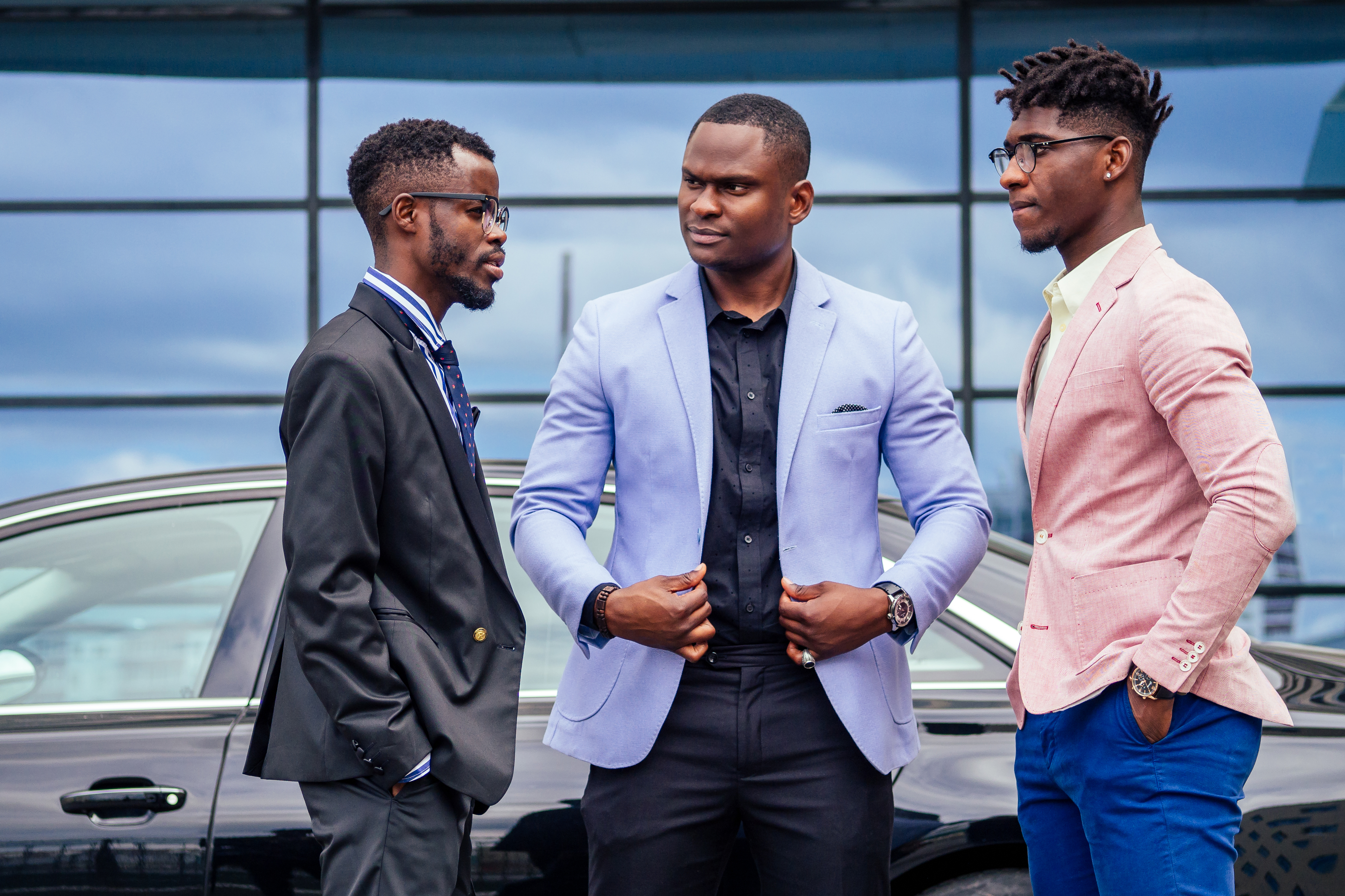 A group of three African Americans business men in stylish suits communicate discussion with each other on the street skyscraper office windows background